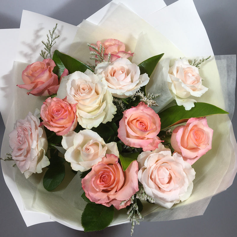 One dozen assorted coloured roses, peaches, pinks and foliage in wet wrap for Valentine's Day