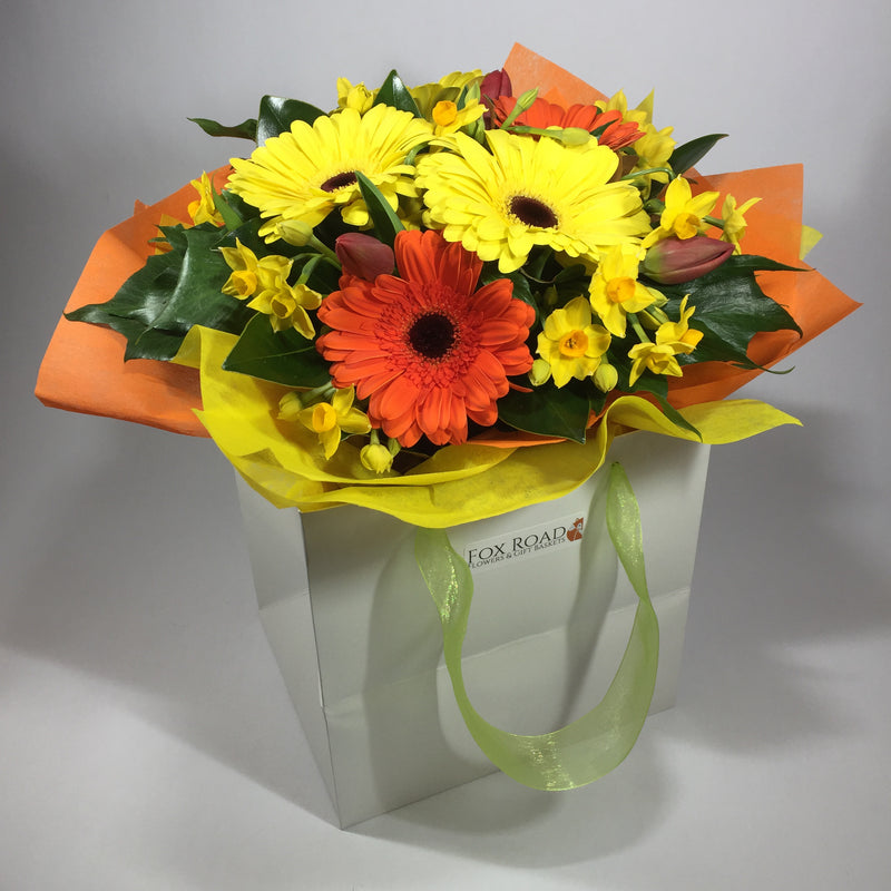 Bright flower gift bag filled with yellow and orange gerberas
